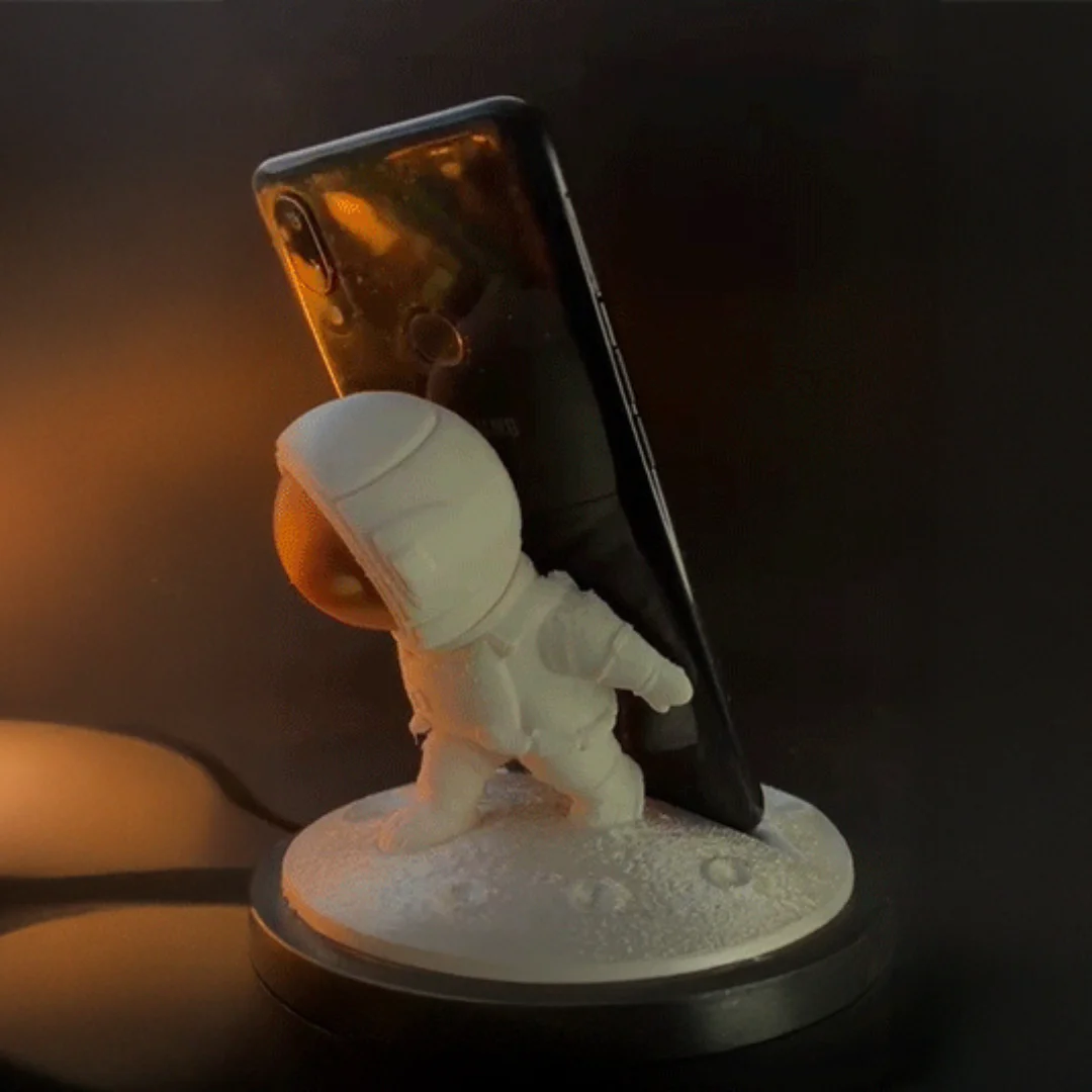 Astronaut phone holder supporting an upright smartphone on a round lunar-style base.