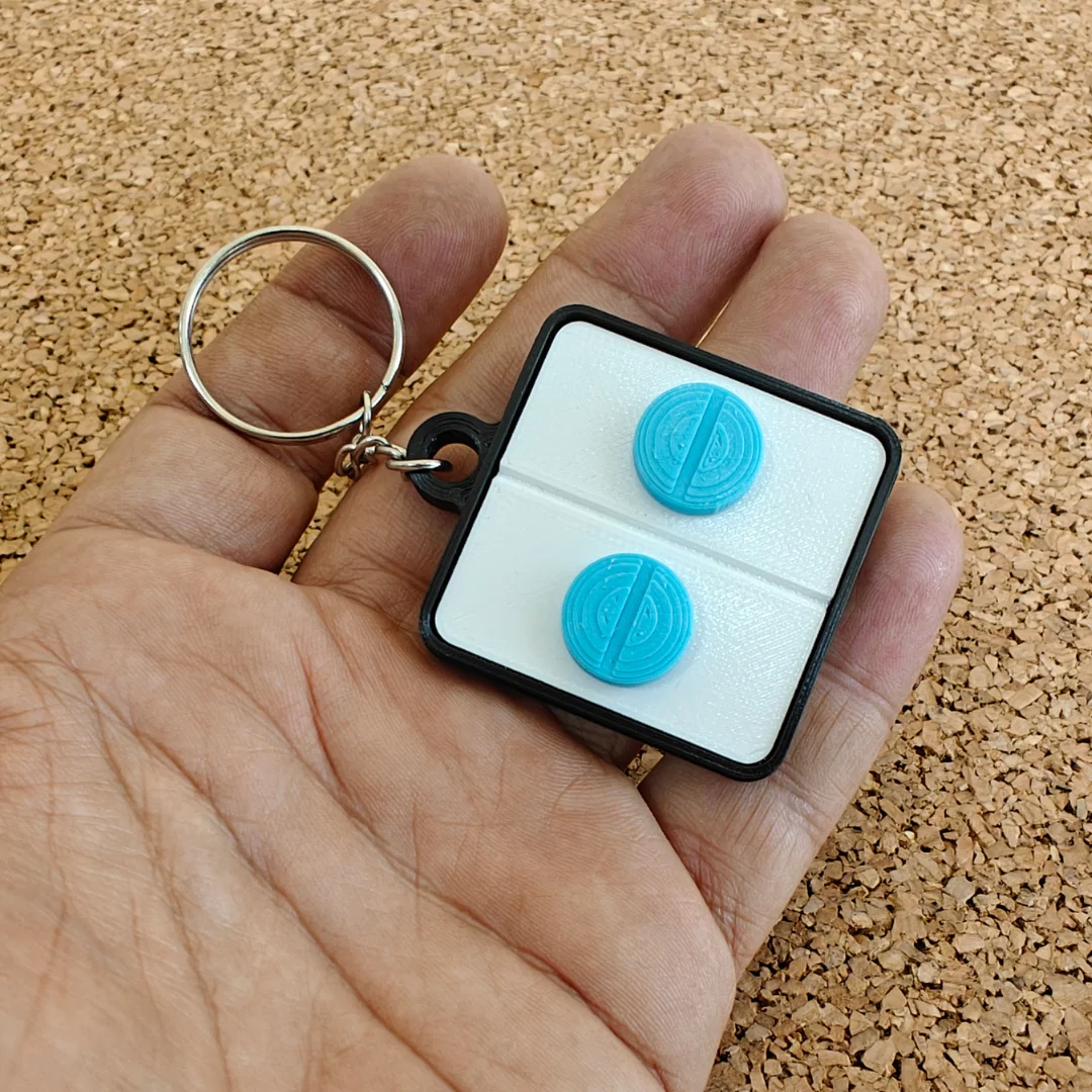 Round pill keychain held in a hand, showing the raised pill details and compact size.