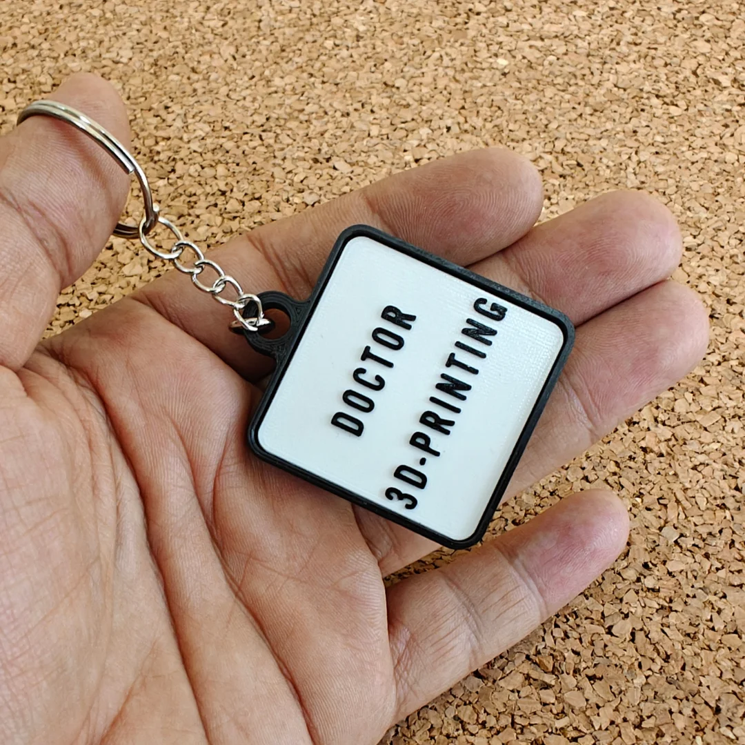 Reverse of the capsule keychain held in a hand, showing raised custom lettering.