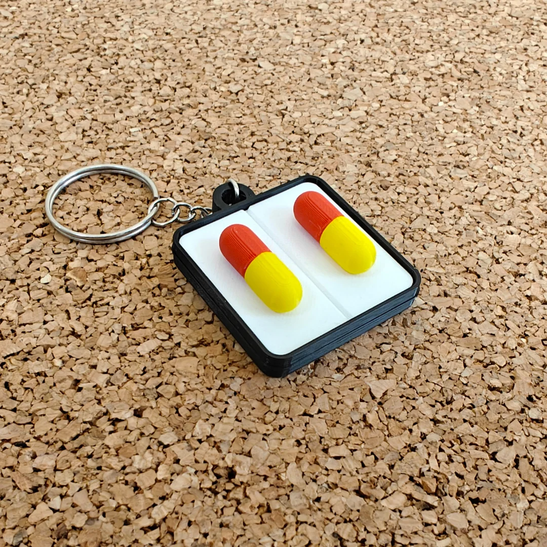Front view of a capsule-themed keychain with two raised capsules and a split ring.