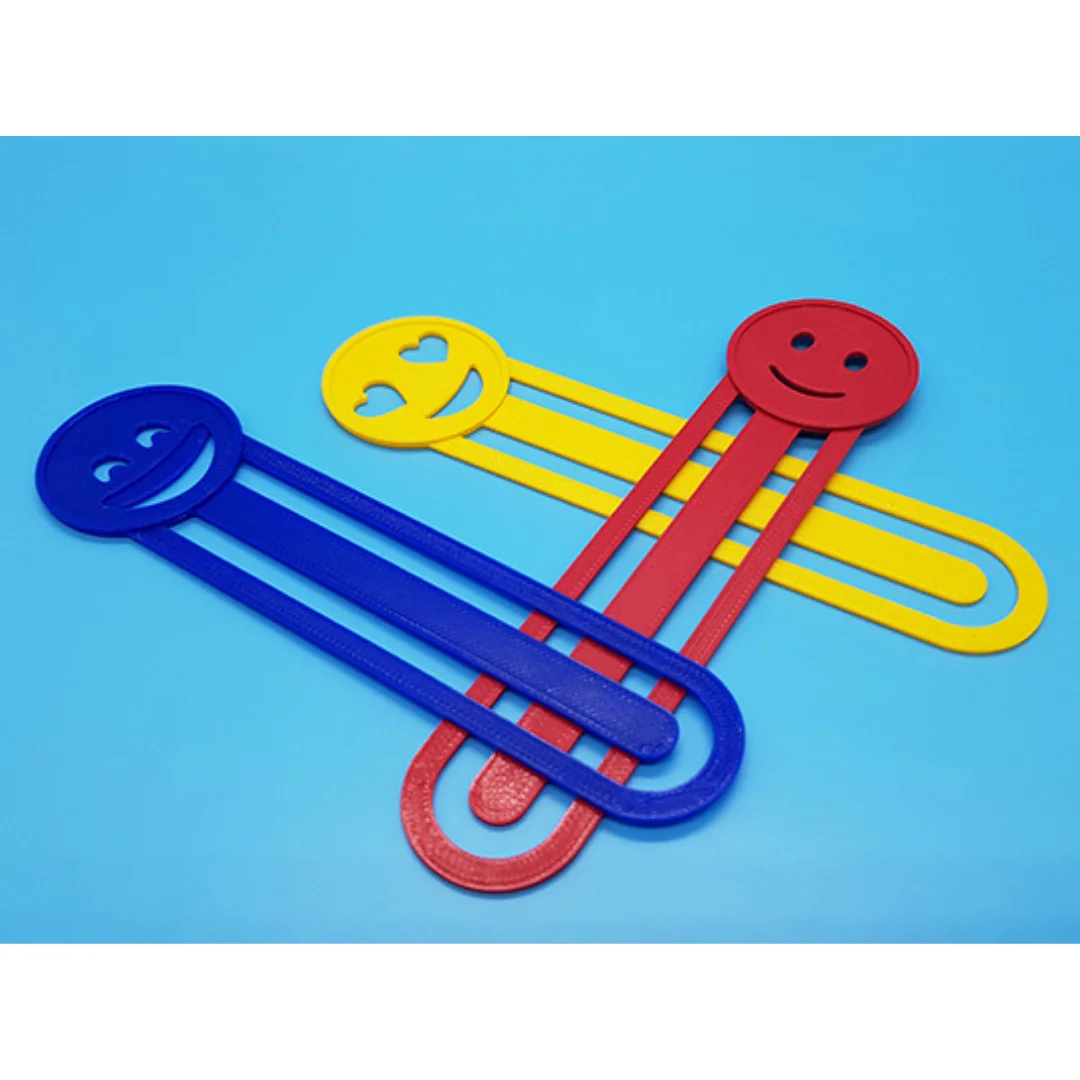 Three 3D printed bookmarks with emoji faces and elongated paperclip-style bodies.