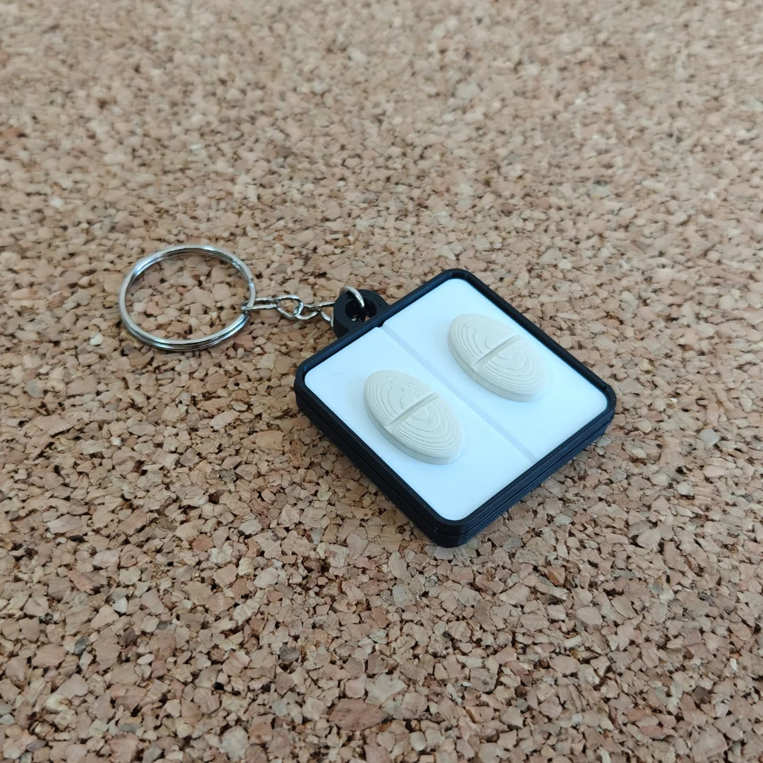 Front view of a rectangular keychain with two oval pill shapes and a split ring.