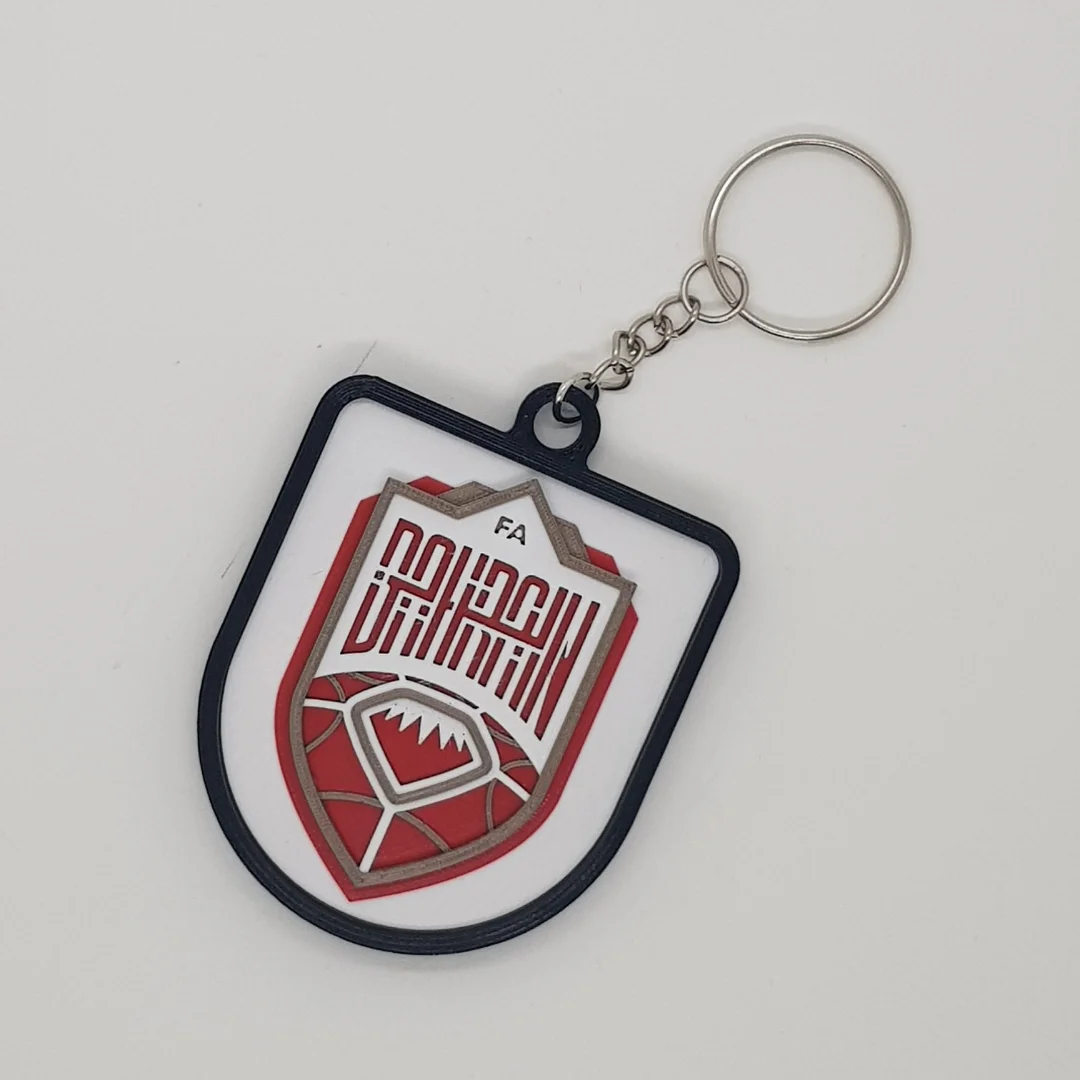 Front view of a Bahrain football crest keychain with its chain and key ring.